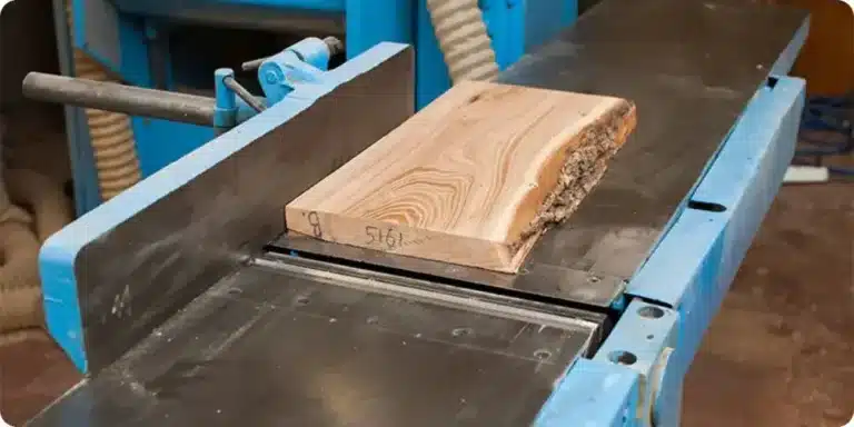 Planche de bois brut posée sur les tables d'une dégauchisseuse avant corroyage — le réglage des tables et des fers détermine la présence ou l'absence de talonnage